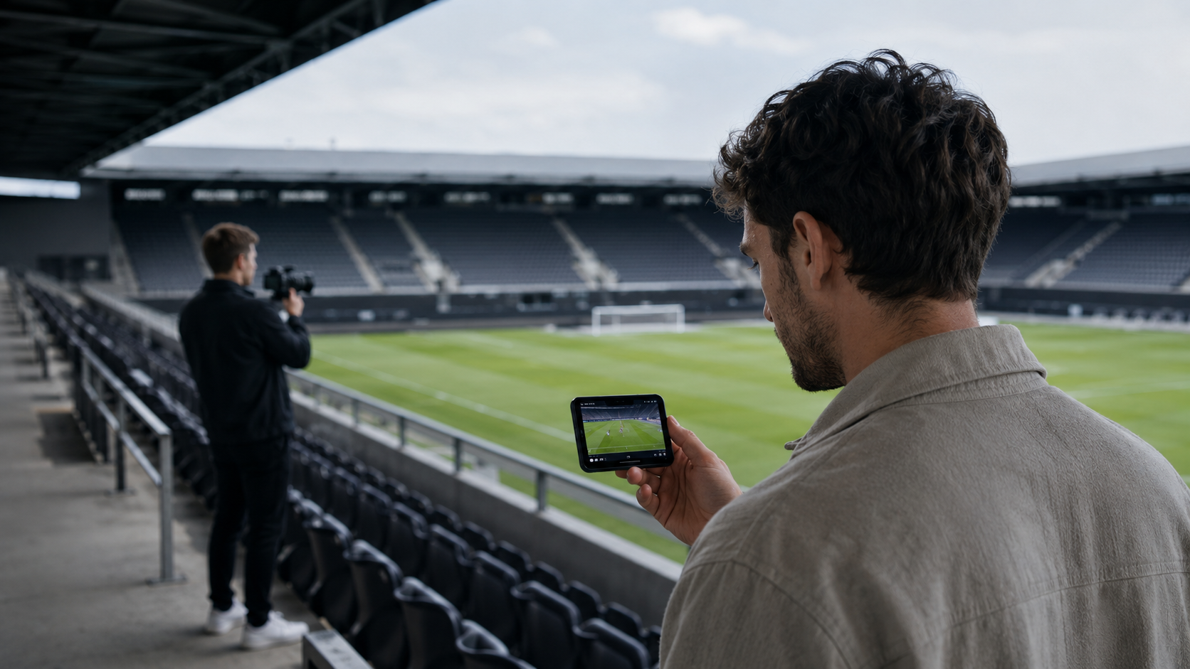 Modern Football Content and Supporter Engagement Supporter watching digital football content while a club media professional films inside a stadium.